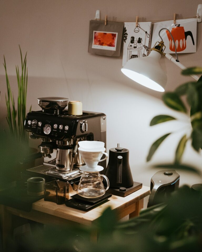 A person pours hot water from a kettle into a ceramic dripper over a glass carafe on a kitchen counter.