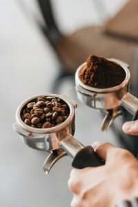 Close-up of several hands holding different varieties of raw and roasted coffee beans on a wooden table.