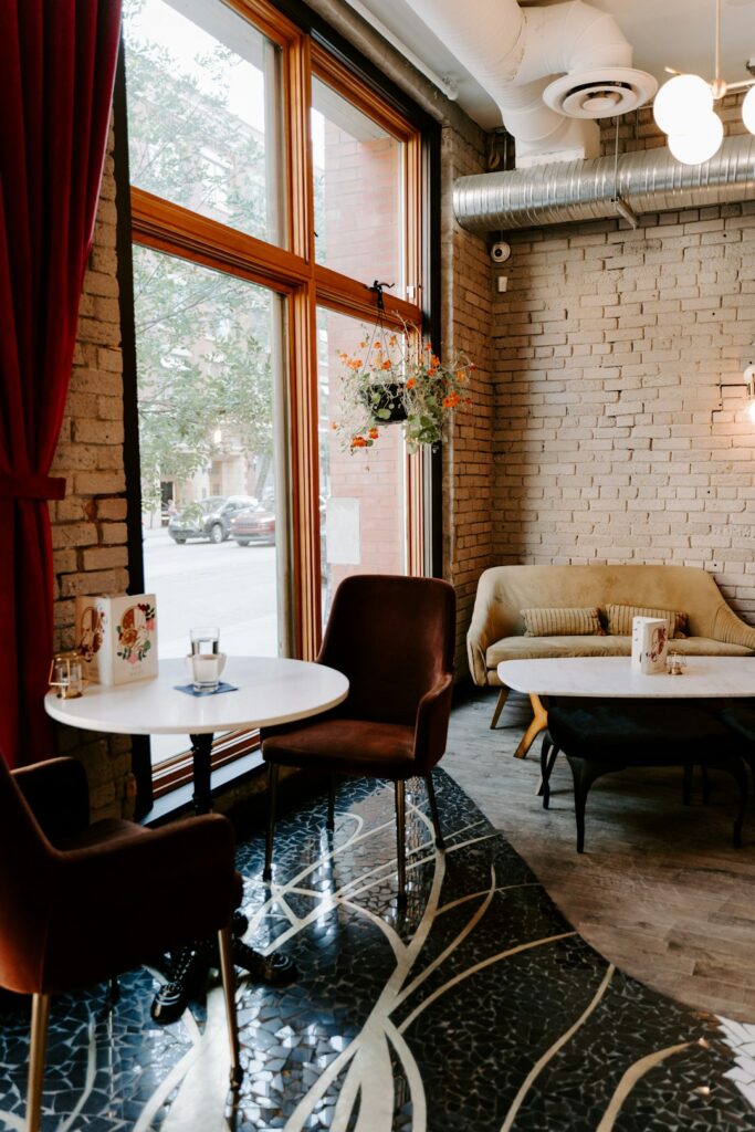 A person relaxing with coffee at a small table by a window, surrounded by warm lighting and simple decor.