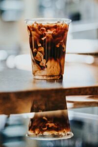 Person reading a coffee menu beside espresso cups, milk options, and a glass of iced coffee.