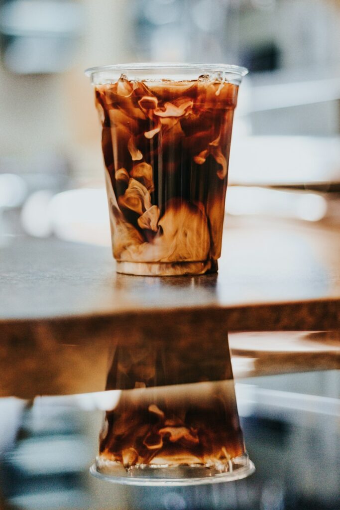 Person reading a coffee menu beside espresso cups, milk options, and a glass of iced coffee.