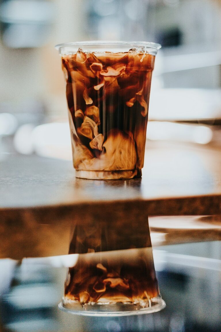 Person reading a coffee menu beside espresso cups, milk options, and a glass of iced coffee.