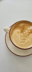 A person holding a milk frothing pitcher above a coffee mug creating simple latte art.
