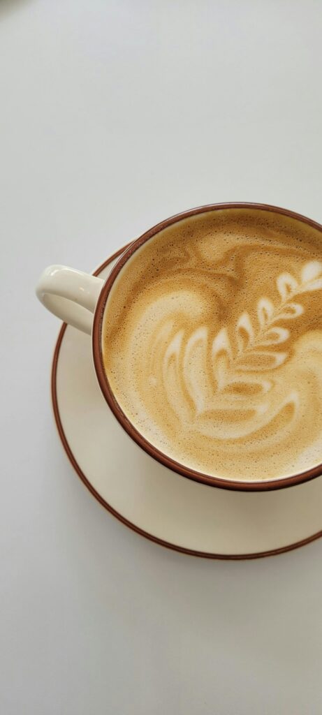 A person holding a milk frothing pitcher above a coffee mug creating simple latte art.